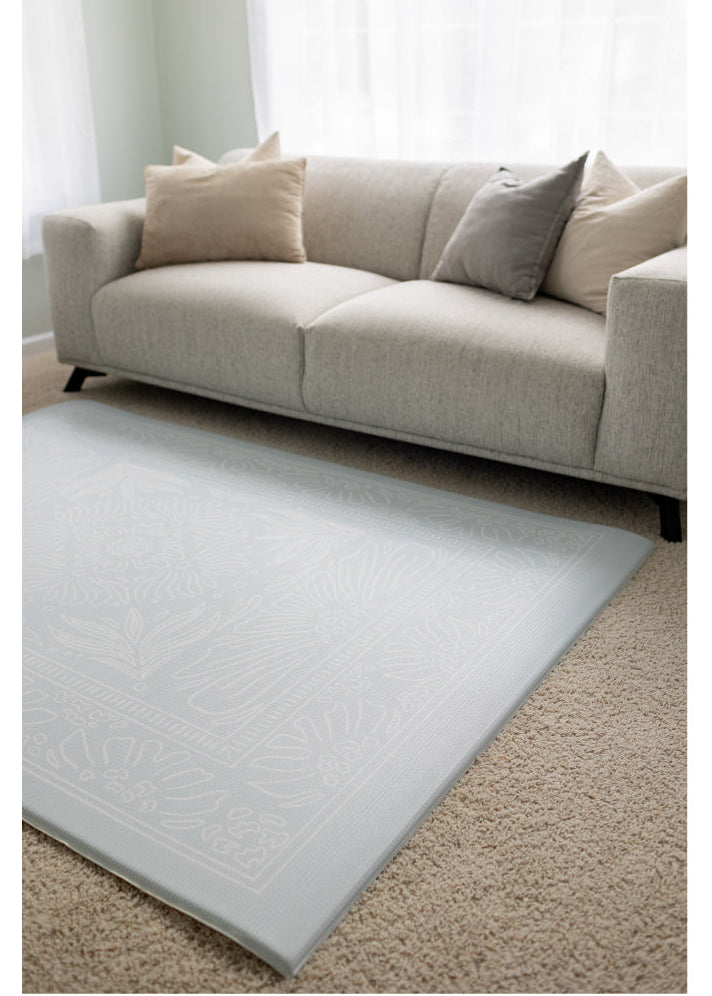 Light blue rug on a beige carpet with a beige sofa in the background