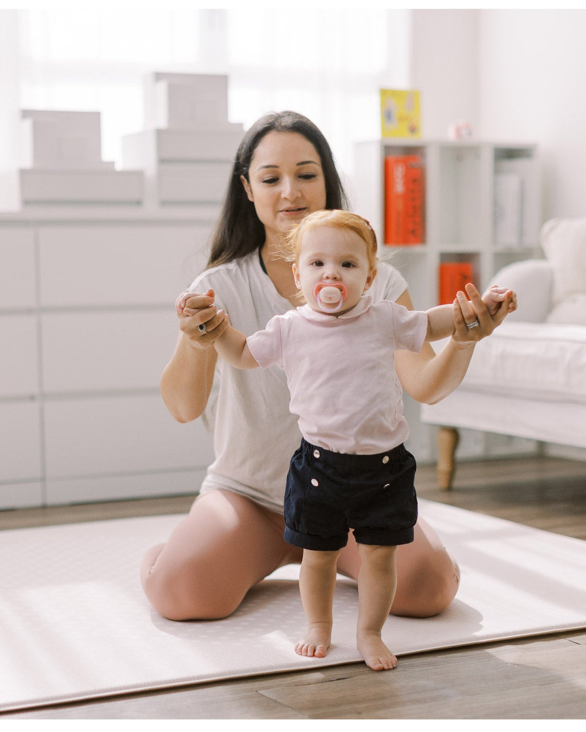 Woman holding a baby on a yoga mat in a home setting