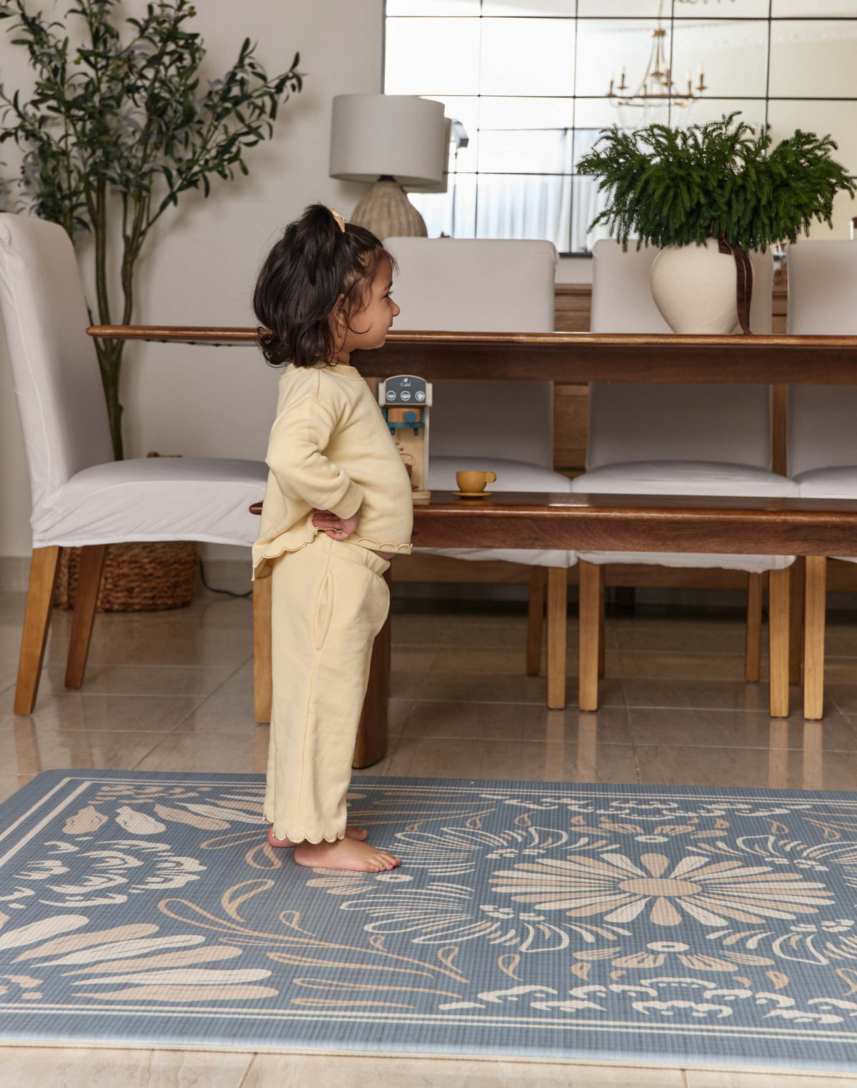 Child standing on a blue floral rug in a modern living room.