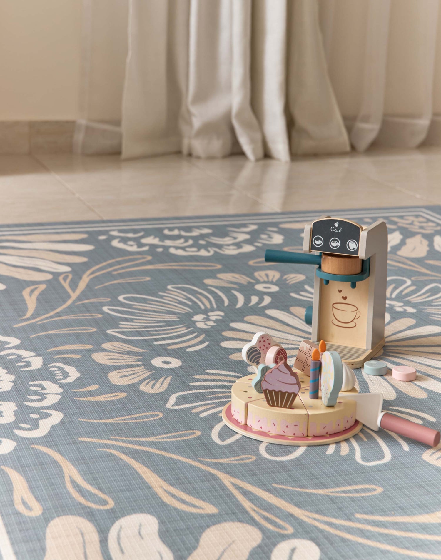 Wooden toy set on a floral-patterned rug with curtains in the background